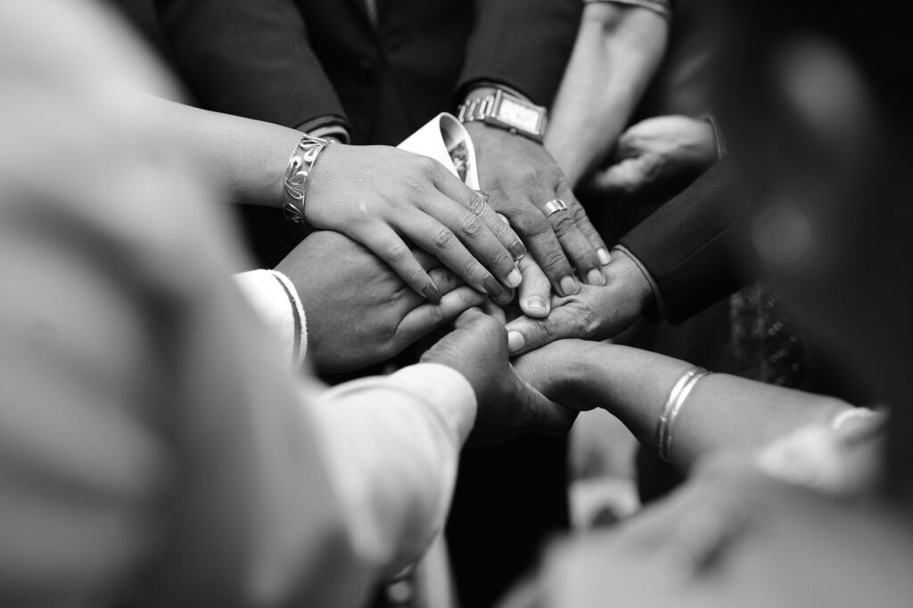 A close-up black and white photo of diverse hands united in prayer, symbolizing spiritual unity