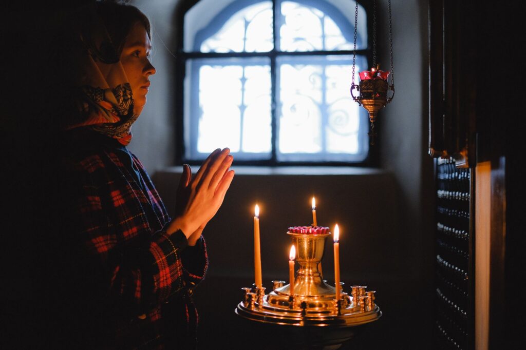 A woman in prayer by candlelight inside a church, conveying peace and contemplation
