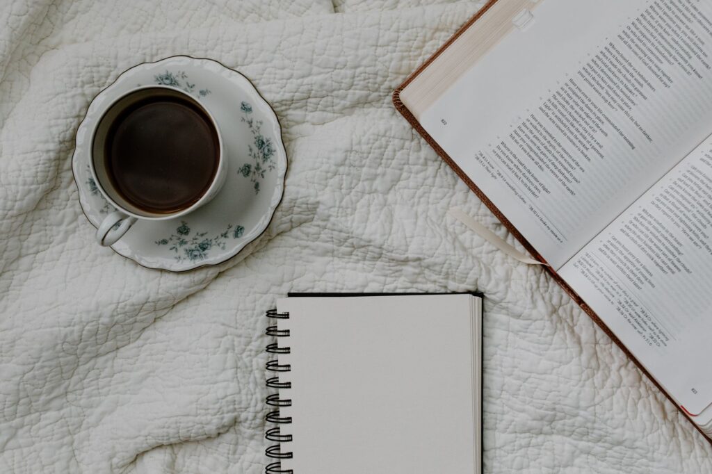 Flat lay of a coffee cup, open Bible, and notebook on a quilted fabric